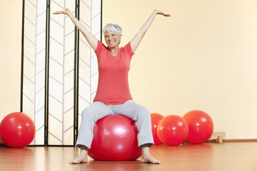 Ältere Frau auf Gymnastikball sitzend, lächelnd, Porträt - WESTF12470