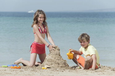 Spain, Mallorca, Children building sandcastle on beach - WESTF12703