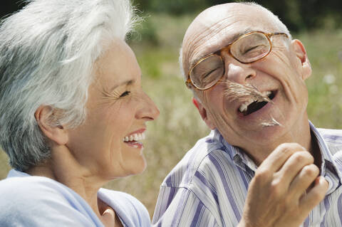 Spain, Mallorca, Senior couple, Woman tickling man with blade of grass, laughing, portrait, close-up stock photo