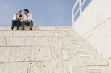 Spanien, Mallorca, Geschäftsleute sitzen auf einer Treppe und halten Dokumente - WESTF12773