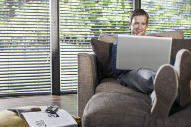 Germany, Hamburg, Man in living room using laptop - WESTF13111