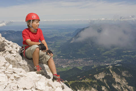 Deutschland, Garmisch-Partenkirchen, Alpspitz, Bergsteiger, Junge (12-13) auf dem Gipfel sitzend, Porträt, lizenzfreies Stockfoto