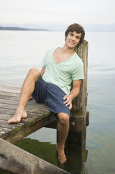 Germany, Bavaria, Starnberger See, Young man relaxing on jetty, smiling, portrait - RNF00069