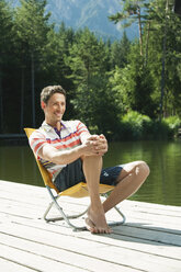 Italy, South Tyrol, Man sitting in chair by lake, portrait - WESTF13304