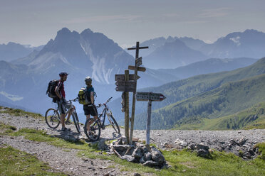 Italy, Dolomites, Mountain bikers standing next to sign posts - FFF01086