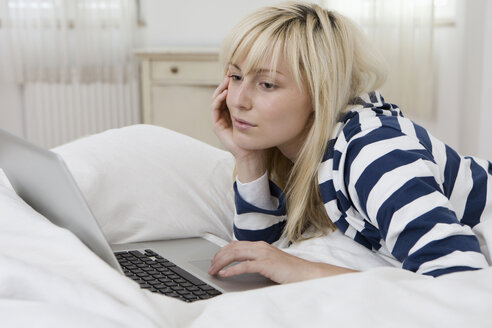 Deutschland, Berlin, Junge Frau im Bett liegend, mit Laptop - WESTF13478