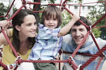 Germany, Berlin, Family at playground looking through climbing net, portrait, close-up - WESTF13598