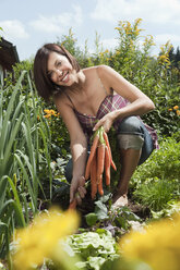 Deutschland, Bayern, Frau hält Karottenstrauß im Garten, lächelnd, Porträt - WESTF13233