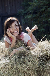 Germany, Bavaria, Woman lying on haystack, smiling, portrait - WESTF13179