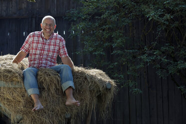 Germany, Bavaria, Senior man sitting on haystack - WESTF13162
