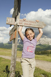 Italy, Seiseralm, Girl (6-7) standing by sign post, smiling, portrait - WESTF13433