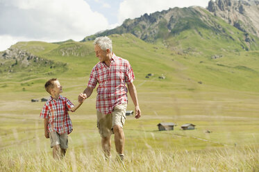 Italy, Seiseralm, Grandfather and grandson (6-7) walking in field - WESTF13390