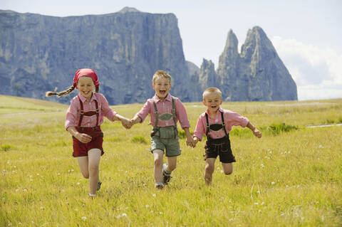 Italien, Seiseralm, Drei Kinder (4-5), (6-7), (8-9) laufen im Feld, lizenzfreies Stockfoto