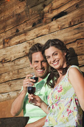 Italien, Südtirol, Paar vor Blockhütte mit Weingläsern, lächelnd, Porträt - WESTF13729
