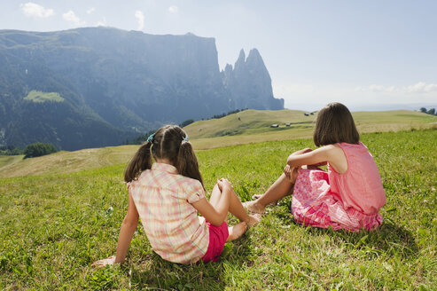 Italien, Südtirol, Seiseralm, Zwei Mädchen (6-7) (10-11) sitzen auf einer Wiese, Rückansicht - WESTF13654