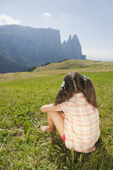 Italien, Südtirol, Seiseralm, Mädchen (6-7) auf einer Wiese sitzend, Rückansicht - WESTF13652