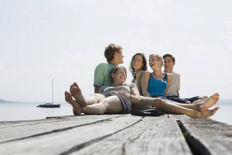 Deutschland, Bayern, Ammersee, Junge Leute sitzen auf Steg, lachend, Porträt, lizenzfreies Stockfoto