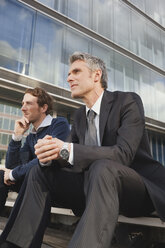 Germany, Hamburg, Two businessmen sitting on steps in front of office building - WESTF13892