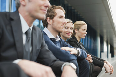 Germany, Hamburg, Four Business people sitting on steps in front of office building - WESTF13883