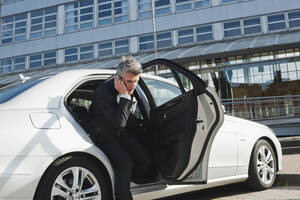 Deutschland, Hamburg, Geschäftsmann benutzt Mobiltelefon, verlässt Auto, Seitenansicht - WESTF13880