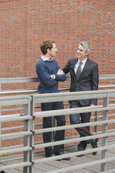 Germany, Hamburg, Two businessmen talking in front of brick wall - WESTF13871