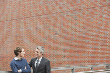 Germany, Hamburg, Two businessmen talking in front of brick wall - WESTF13869