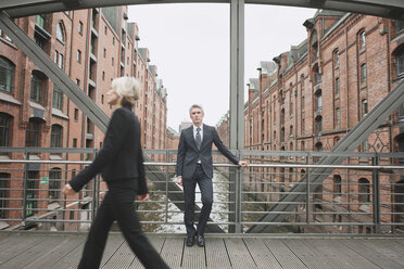 Germany, Hamburg, Businesswoman crossing bridge, Businessman in background leaning against railing - WESTF13865