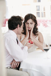 Couple sitting at table in restaurant, man holding gift parcel - WESTF13825