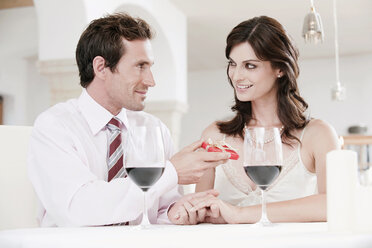 Couple sitting at table in restaurant, man holding gift parcel - WESTF13824