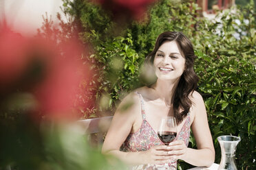 Italien, Südtirol, Frau im Garten mit einem Glas Rotwein in der Hand, wegschauend - WESTF13767