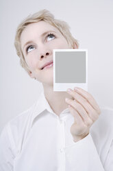 Woman holding polaroid picture, looking up, portrait - TCF01268