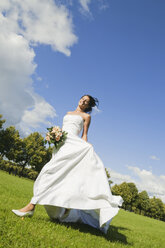 Germany, Bavaria, Bride running in park, holding bunch of flowers, smiling, low angle view - NHF01168