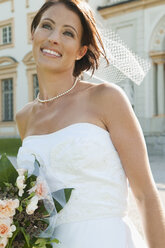 Germany, Bavaria, Bride holding bunch of flowers in front of building, portrait, close-up - NHF01156