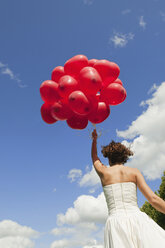 Deutschland, Bayern, Braut hält rote Luftballons, im Freien, Rückansicht - NHF01147