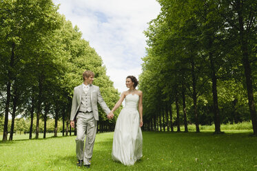 Germany, Bavaria, Bridal couple in park walking hand in hand, smiling, portrait - NHF01146