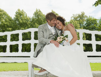 Germany, Bavaria, Wedding couple on bench, outdoors, smiling, portrait - NHF01140