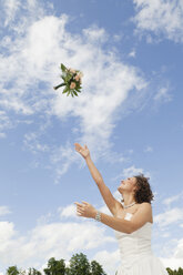 Germany, Bavaria, Young bride throwing a bouquet into the sky - NHF01125