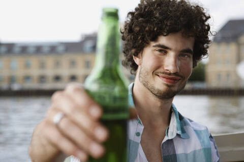 Germany, Berlin, Young man holding bottle, portrait, close-up stock photo