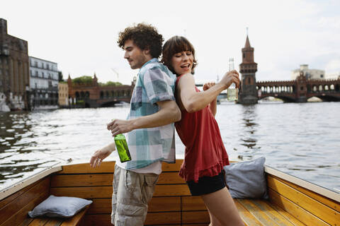 Germany, Berlin, Young couple on motorboat, holding bottles, standing back to back stock photo