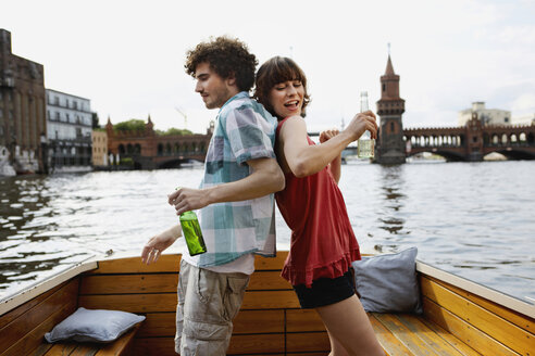 Deutschland, Berlin, Junges Paar auf Motorboot, mit Flaschen in der Hand, Rücken an Rücken stehend - VVF00052