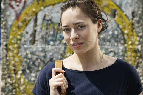 Deutschland, Berlin, Junge Frau vor Mauer mit Graffiti stehend, Portrait, Nahaufnahme, lizenzfreies Stockfoto