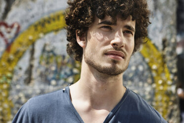 Germany, Berlin, Young man standing in front of wall with graffiti, portrait, close-up - VVF00046