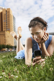 Deutschland, Berlin, Junge Frau liegt auf einer Wiese und benutzt ein Mobiltelefon, Porträt - VVF00033