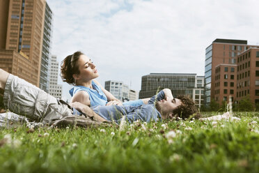 Deutschland, Berlin, Junges Paar liegt auf einer Wiese, Hochhäuser im Hintergrund - VVF00031