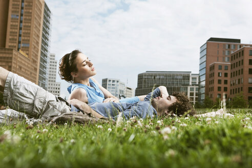 Germany, Berlin, Young couple lying in meadow, high rise buildings in background - VVF00031