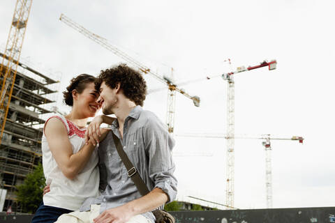 Deutschland, Berlin, Junges Paar vor neuem Gebäude, Kräne im Hintergrund, lizenzfreies Stockfoto