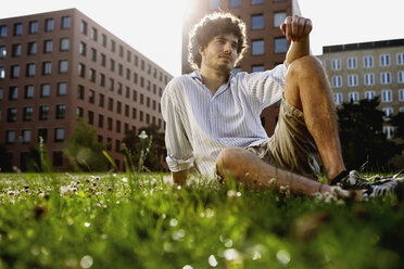 Deutschland, Berlin, Junger Mann entspannt auf Rasen, im Hintergrund Hochhäuser - VVF00010