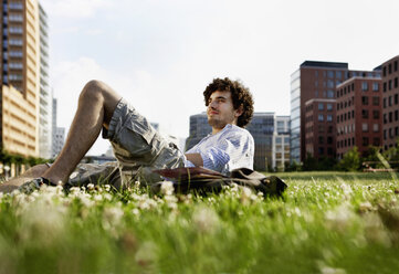 Germany, Berlin, Man relaxing on lawn, in background high rise buildings - VVF00009