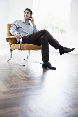 Geschäftsmann sitzt auf einem Stuhl und benutzt ein Mobiltelefon, lizenzfreies Stockfoto