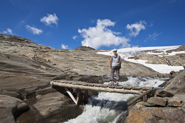 Austria, Grossglockner, Woman standing on Wooden bridge over mountain stream - FOF01917